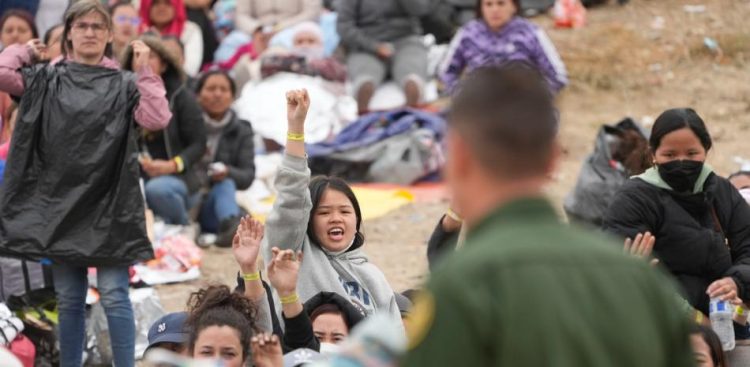 Las mujeres sostienen sus pulseras en alto con la esperanza de que los agentes de la Patrulla Fronteriza de EE. UU. las elijan para ser procesadas después de esperar días entre dos muros fronterizos.AFP