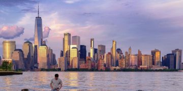 Un hombre comprueba dónde pisa mientras camina por el agua en el Canal Morris en Jersey, Nueva Jersey, mientras se pone el sol con Manhattan de fondo, el 31 de mayo de 2022.J. DAVID AKE / AP